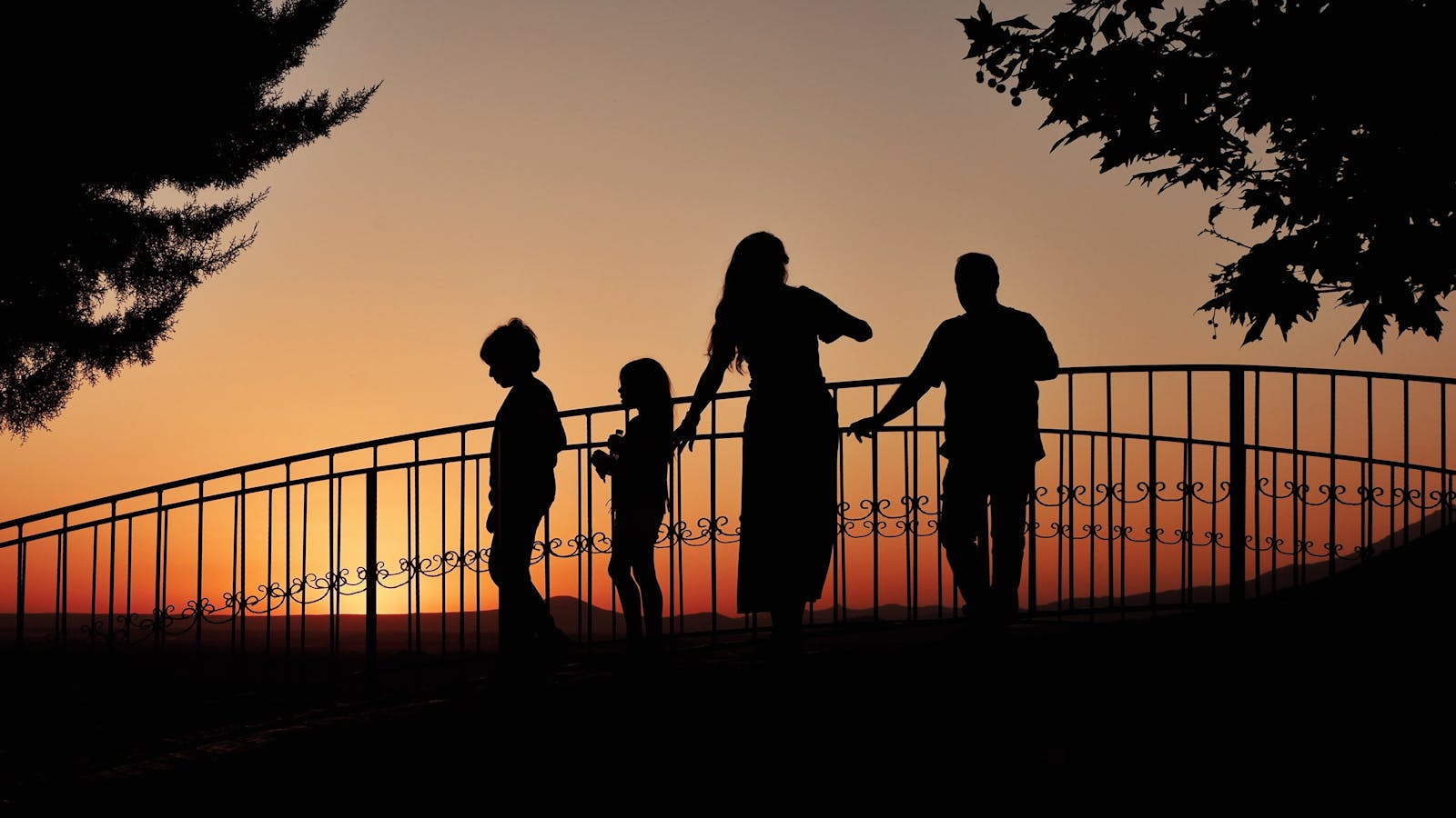 Silhouettes of a Family Standing on a Bridge at Dusk
